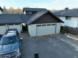 Two-car garage with gabled roof, white doors, and concrete driveway