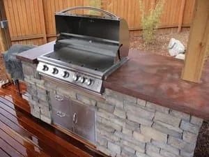 Stainless steel grill with stacked stone island base and composite countertop on wooden deck