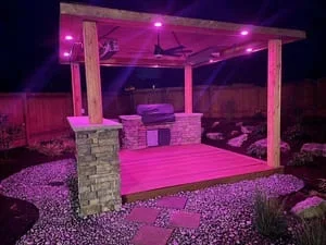 Wooden pavilion with stone columns, LED ceiling lights, and gravel landscaping at night