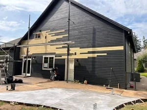 Home addition with black siding, yellow beam supports, and concrete patio foundation